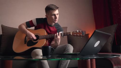 Young Adult Plays Guitar and Looks at Laptop