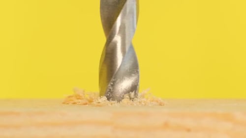 A Drill is Screwed Into a Wooden Board on a Yellow Background Vertical Video