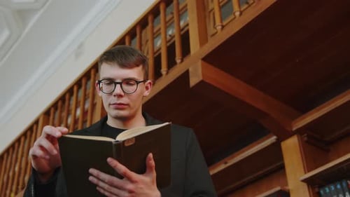 Young Man Engrossed in Reading Within a Quiet Library Environment with Books Surrounding Him Media