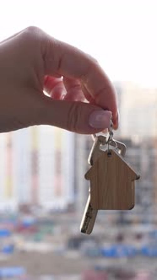 Key with House Keychain in Hand on Background with New Houses Construction House Purchase and Real