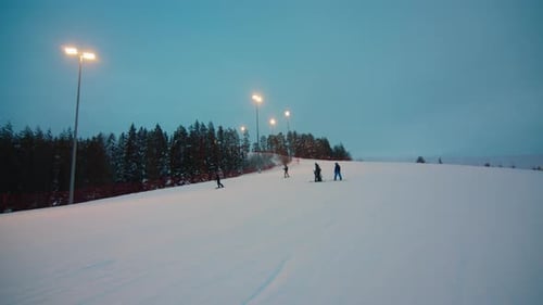 People go downhill on the slope of the skiing center at sunset