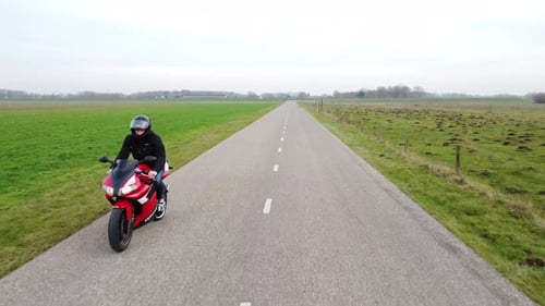 Shot of motorcyclist driving down a road with drone in front of him.
