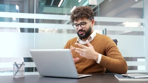 Confident businessman talking on a video call conference using a laptop sitting at workplace