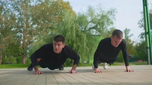 Two young men do push-ups in an urban park