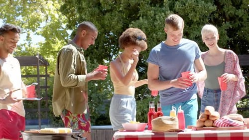 Happy diverse group of friends drinking drinks and having barbecue in garden in summer