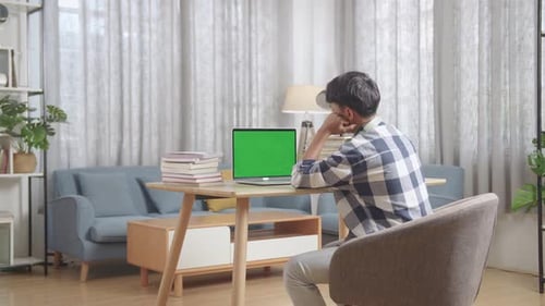 Bored Teenage Boy Learning Online From Laptop With Green Mock Up Screen At Home