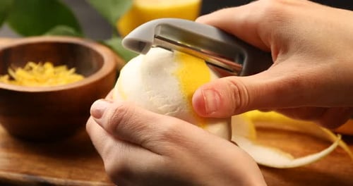Woman peeling lemon zest at table, closeup