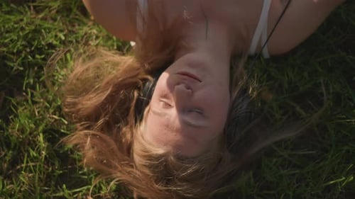 Woman Listens to Music Lying on Grass