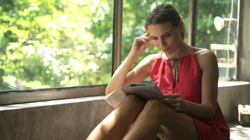 Young woman enjoys morning leisure reading a magazine by the window at home