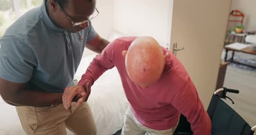 Young Adult Helping Senior Man Into Wheelchair