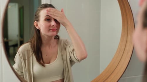 Eine schöne langhaarige Frau schaut in den Spiegel und berührt ihr Gesicht, indem sie Feuchtigkeit spendet
