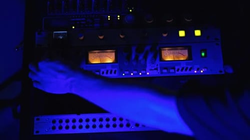 Studio recording equipment in the blue light. Male audio engineer’s hand working on the stereo panel