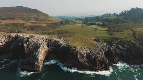 Drone ascends over rugged coastal cliffs, tilting camera downward to reveal rocky shoreline and