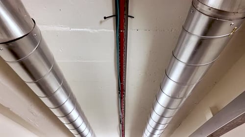 Une paire de tuyaux et de câbles métalliques traversent un plafond blanc.