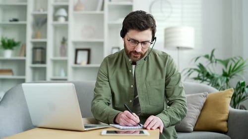 Man Attending Virtual Meeting At Home and Taking Notes