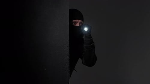 Person in Balaclava with Flashlight Hiding in Dark