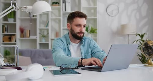 Serious young bearded businessman is typing on a laptop, works online, writes email