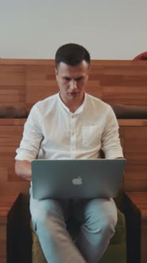 A Man in a White Shirt Sits on a Chair Using an Apple Laptop