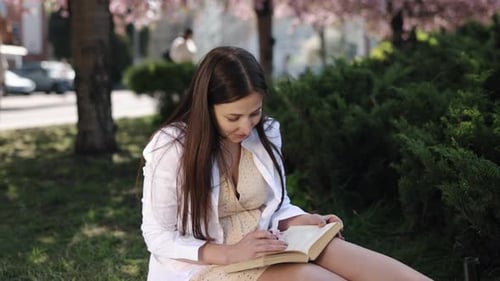 Woman Reading and Smelling Flower in Sunny Park