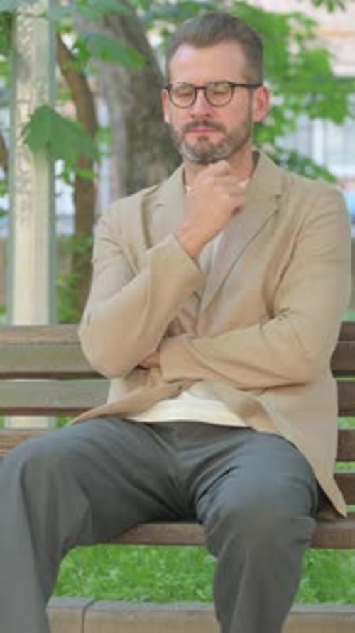 Pensive Young Man Sitting Outdoor on Bench, Vertical Video