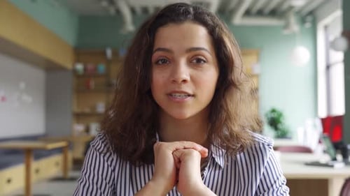 Happy young latina teacher talks to camera at virtual class in home office