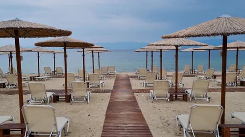 Walking between wooden parasols and empty sunbeds on a sandy beach.