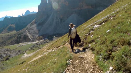 Blonde women walking breathtaking mountain trial in Dolomites; following shot
