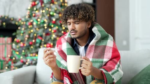 Ill Person Wrapped in Blanket Holding Thermometer