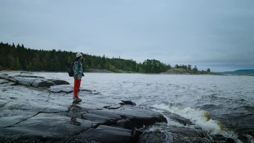 Female Person Standing Alone On Stone Shore Of Beautiful Lake Admiring Nature In Cloudy Day