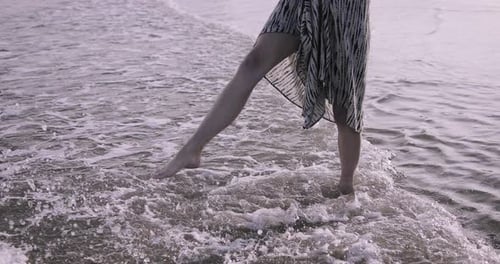 Young adult woman splashing water in the sea in dress