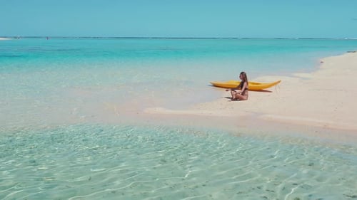 Young Woman Meditating on a Sandbank in the Maldives with a Kayak