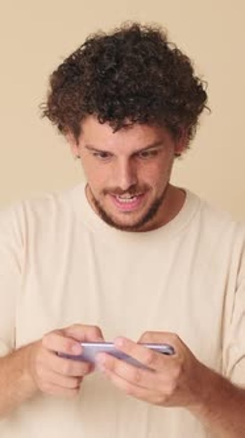 Man playing online video game, wins, waves hands triumphantly in studio on beige background
