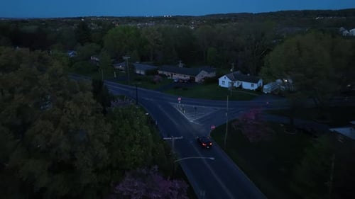 Black car at intersection not stopping at stop sign on street in American suburb. Dusk shot in rural