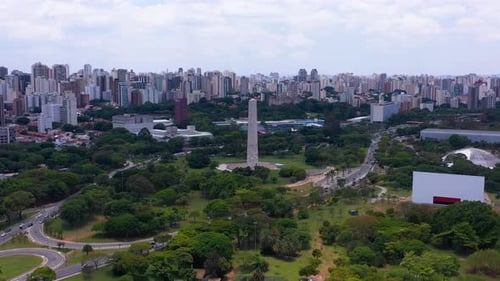 Pullback from Obelisk of Ibirapuera surrounded by vegetation, Sao Paulo skyline as background
