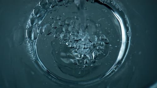 Refreshing water pouring into a transparent cup bubbles exploding super slow motion