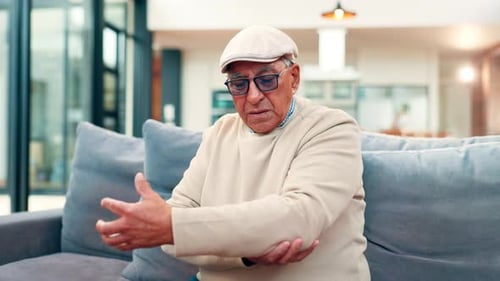 Senior Man Massaging Elbow Indoors on Couch
