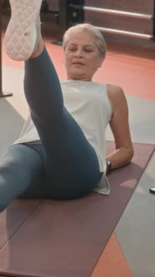 Vertical of Fit Mature Woman Doing Leg Lifts in Gym