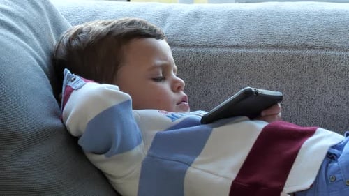 Lindo bebé relajándose en el sofá viendo películas en el teléfono inteligente