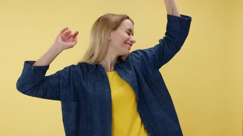 Overjoyed Woman Raising Arms Upwards and Moving Over Yellow Studio Background