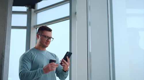 Adult Man Using Phone, Holding Coffee Indoors