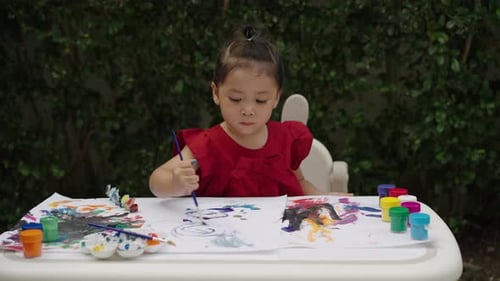 happy toddler girl painting watercolor in a paper at backyard