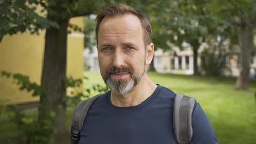 Man with Beard and Backpack Smiles in City Park