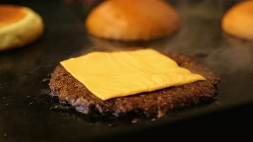 Melted Cheese Bubbling on Burger Patty with Buns Toasting on Grill Background