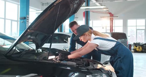 Mechanic in Uniform Repairing Car Motor and Female Filling in Bill Document in Auto Service Young