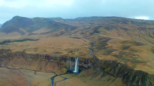 Drone shot over large waterfall flowing down massive Icelandic valley