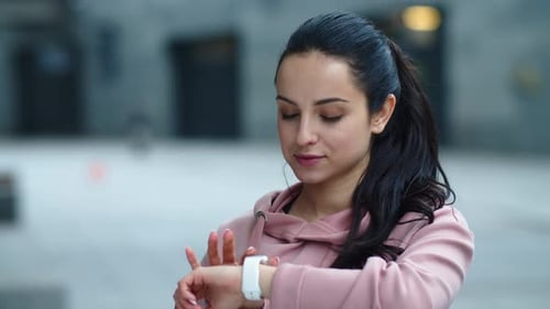 Attractive fitness woman reads message on smart watch in city street slow motion