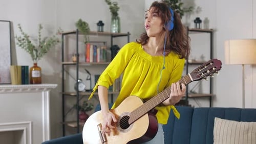 Woman Plays Guitar and Sings with Headphones at Home