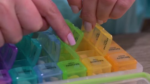 Woman carefully placing prescribed medications in pill organizer, organizing daily pills