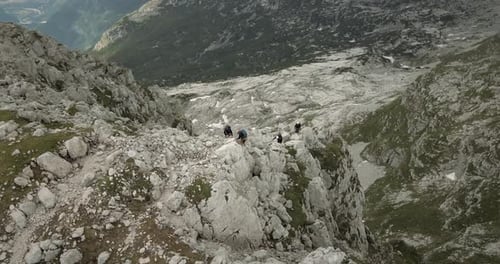 A group of hiker climbing up on rocks towards the top of mountain Rombon. Birdseye perspective, look