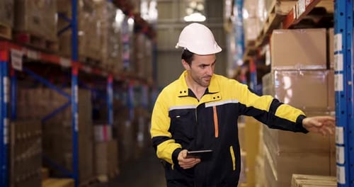 Male warehouse staff with digital tablet in hand checks shipment details beside stacked cargo boxes